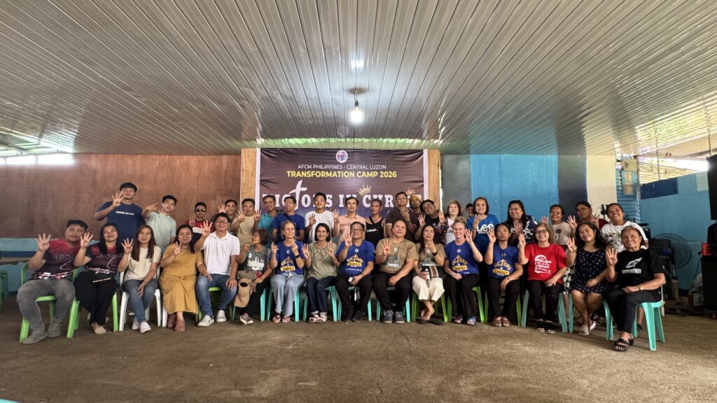 The same group of leaders from the previous photo, but this time everyone is holding up four fingers (the "four" sign) toward the camera, likely signifying a specific camp theme or year.
