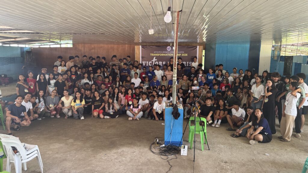 A massive group photo of all camp participants—youth and staff—filling the hall. They are sitting and standing together in front of the main event banner, smiling for the camera.