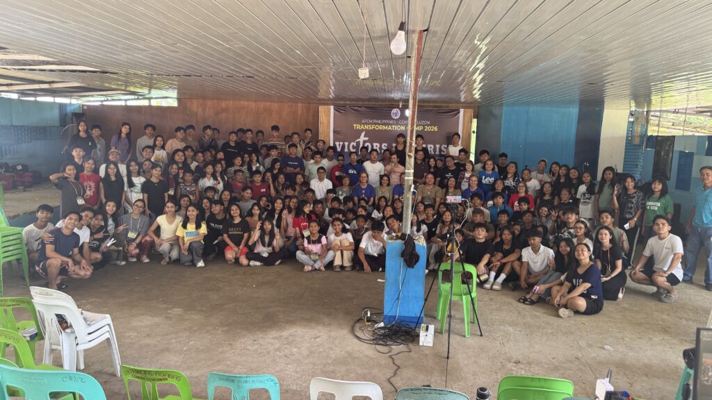 A massive group photo of all camp participants—youth and staff—filling the hall. They are sitting and standing together in front of the main event banner, smiling for the camera.